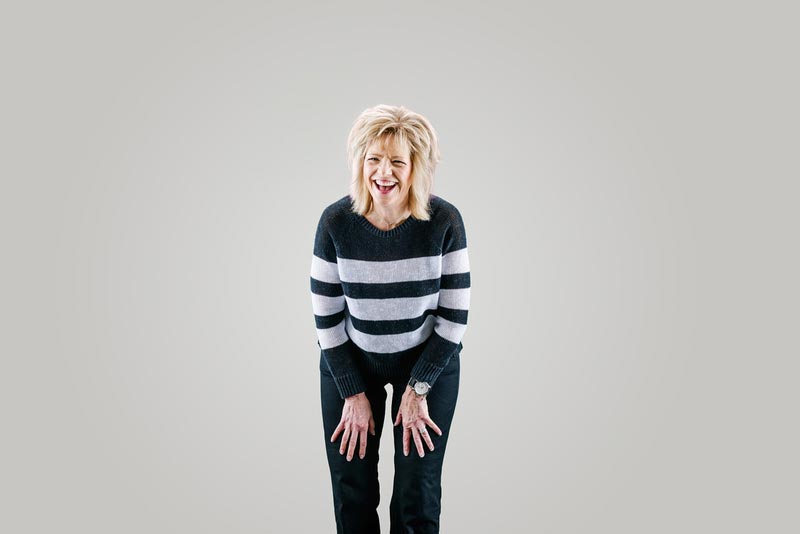 A woman in a striped sweatshirt and vibrant scarf joyfully smiles